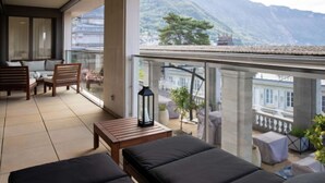 A balcony with a sofa, chairs, and a table, overlooking a mountainous landscape.