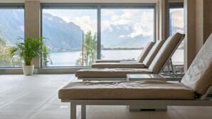 A modern lounge area with large windows offering a view of a lake and mountains.
