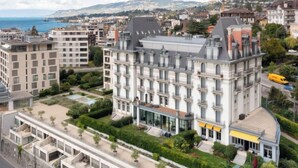 A multi-story hotel with a classic architectural style, featuring a central courtyard and a view of the sea.