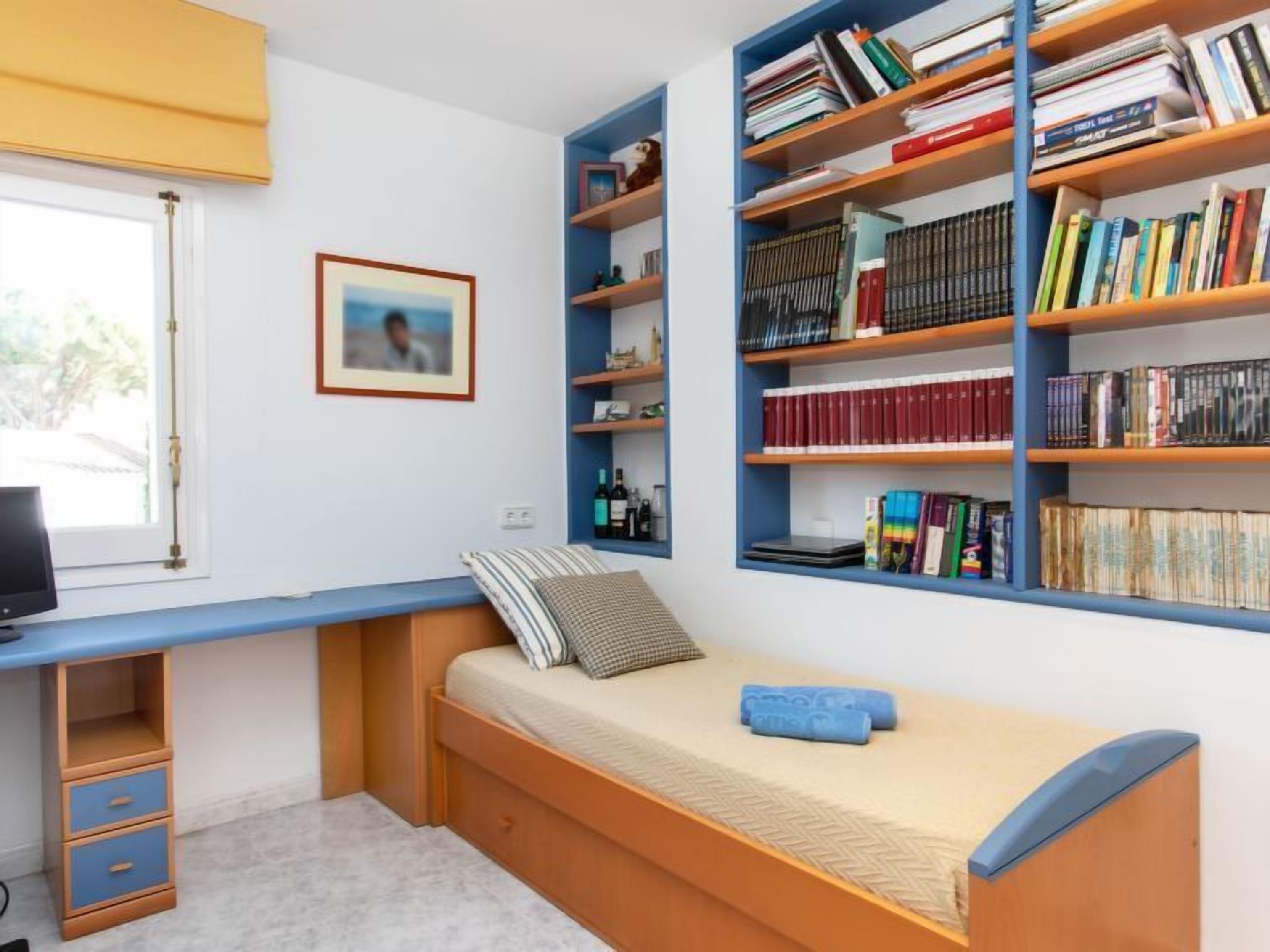 A compact bedroom with a single bed, a desk, and a bookshelf filled with books.