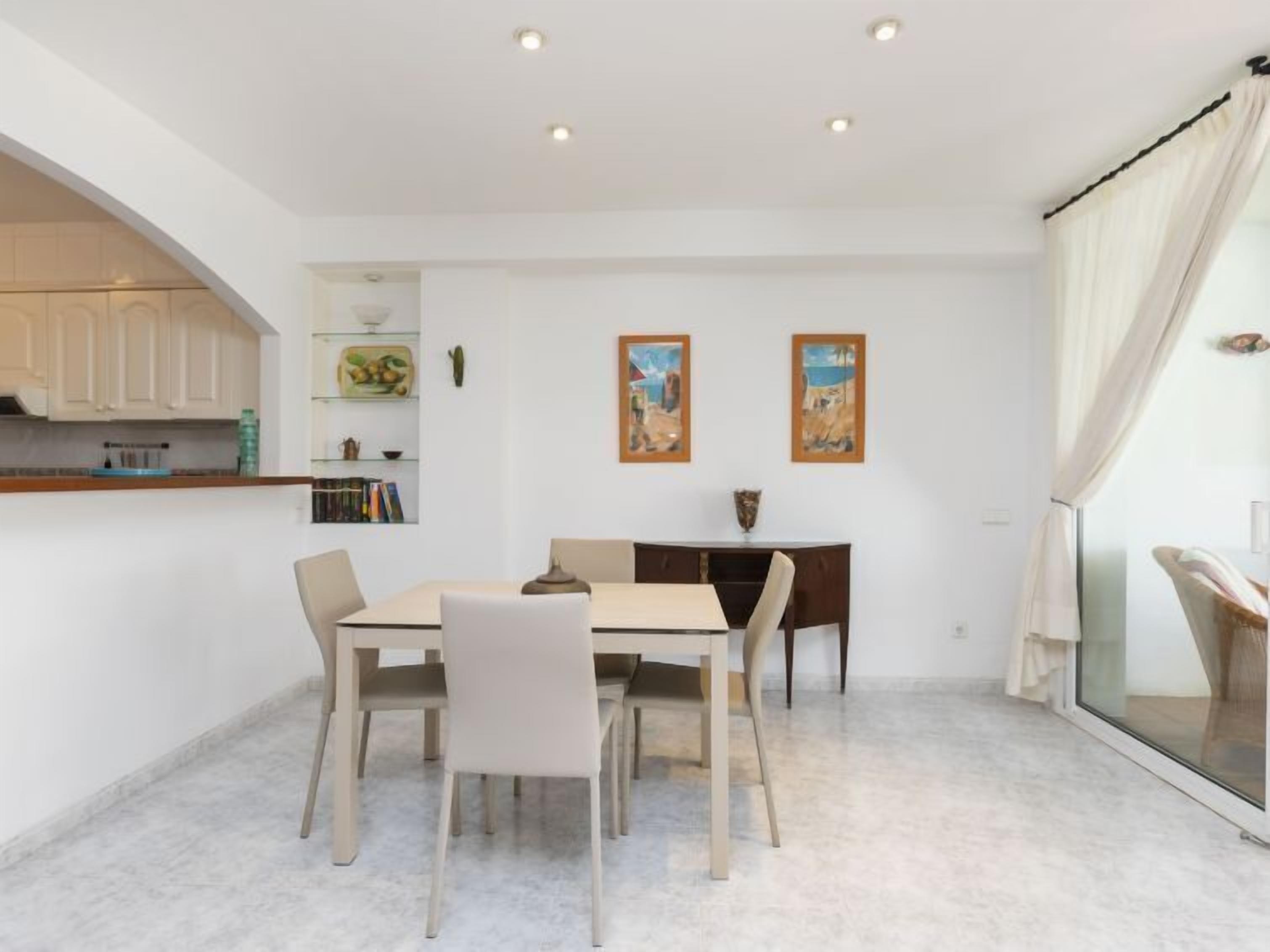 Un espace de salle à manger moderne avec une table et des chaises, une cuisine équipée de meubles de rangement et des œuvres d’art accrochées aux murs.
