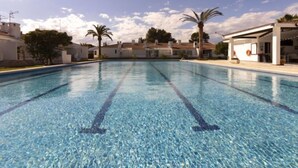 Une piscine à l’eau d’un bleu cristallin, entourée de bâtiments blancs et de palmiers.