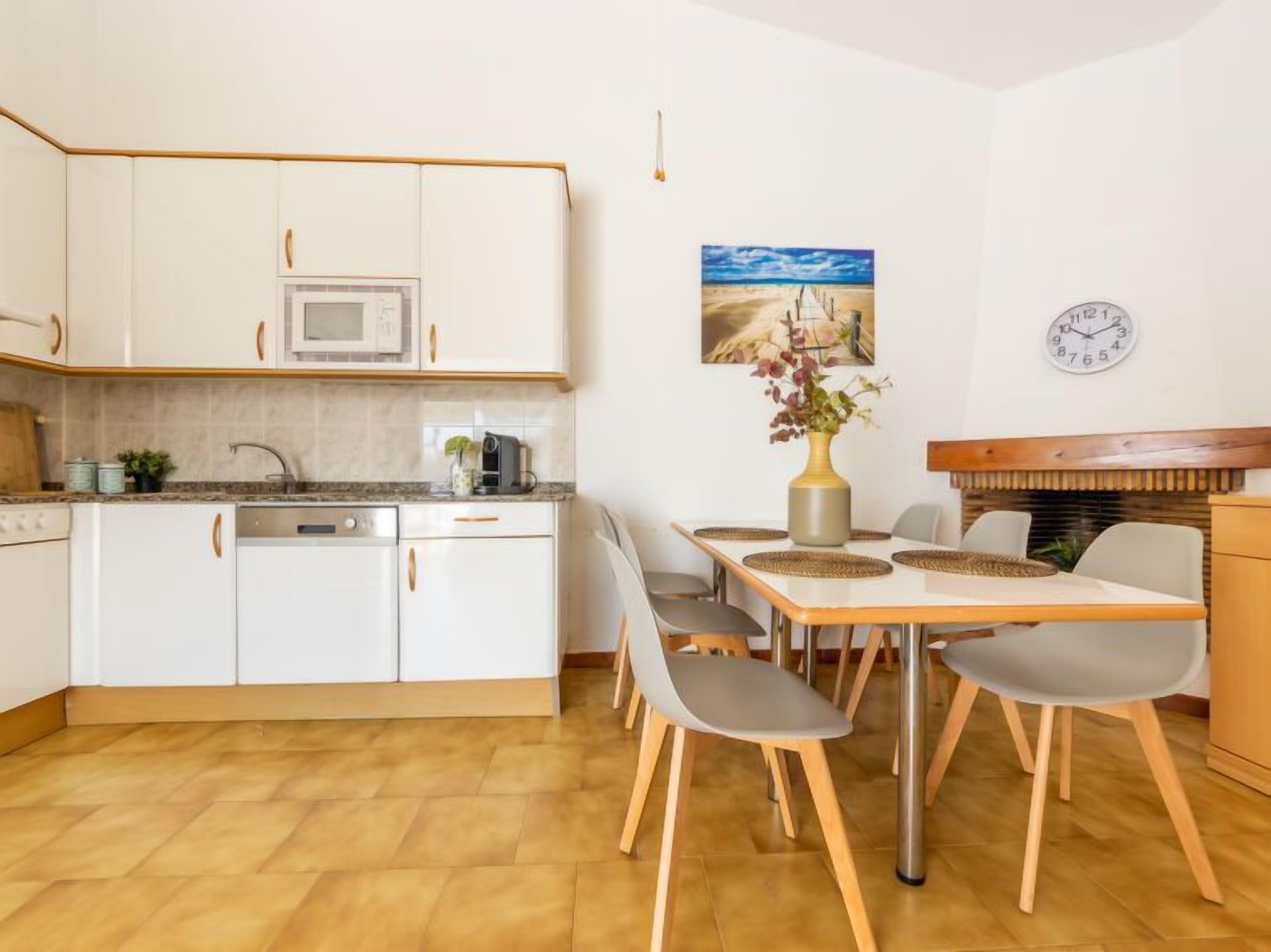 A modern kitchen with white cabinets, a microwave, and a dining area with a wooden table and chairs.