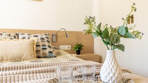 Un lit bien fait, agrémenté d’oreillers à motifs, une table de chevet avec une lampe, une petite plante en pot et un vase rempli de fleurs.