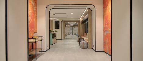 A modern hotel corridor with a central walkway, seating areas, and a reception desk.