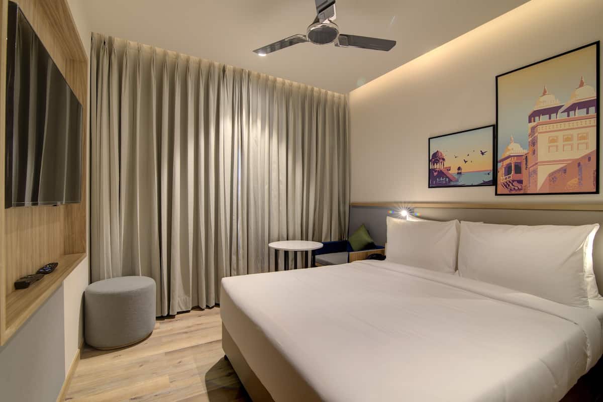 Ein modernes Hotelzimmer mit einem großen Bett, einem Deckenventilator, einem kleinen runden Tisch und zwei gerahmten Bildern an der Wand.