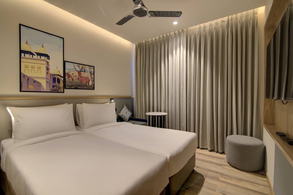 Ein Hotelzimmer mit einem großen Bett, einem Deckenventilator, einem Fernseher und einem Fenster mit Vorhängen.