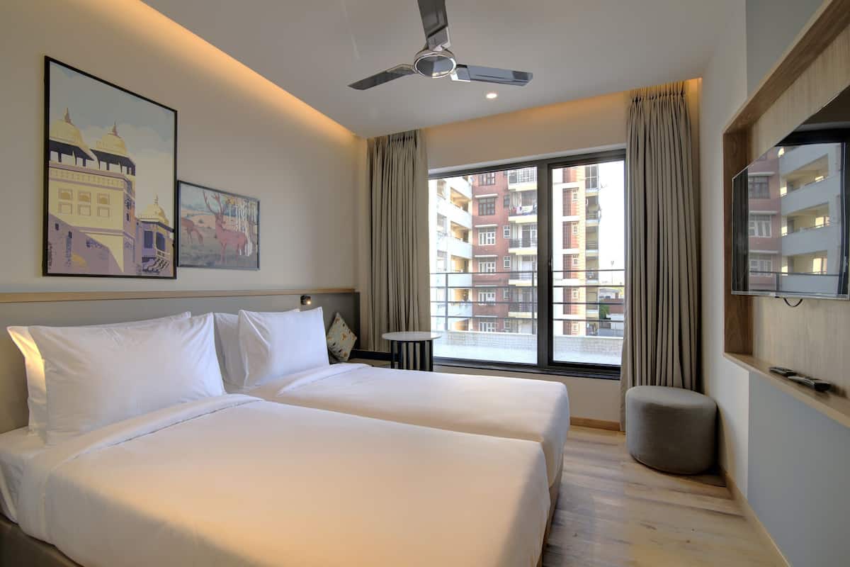 Ein Hotelzimmer mit zwei Betten, einem Deckenventilator, einem großen Fenster mit Vorhängen und Bildern an der Wand.