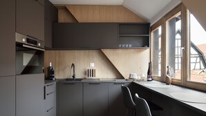 Een moderne keuken met donkere kastjes, een houten aanrecht en een raam met uitzicht op een gebouw.