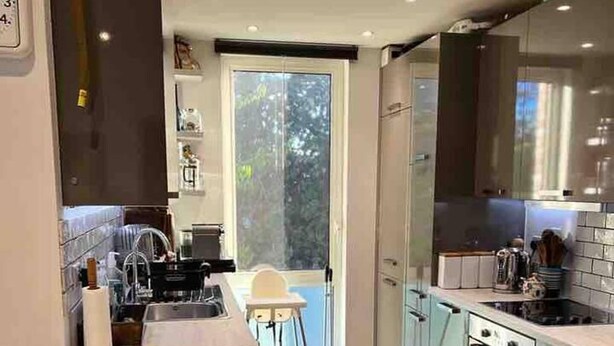Une cuisine moderne dotée d’un îlot central, d’un coin repas et offrant une vue sur l’extérieur grâce à une porte vitrée.