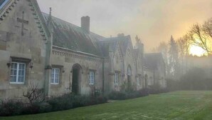Un bâtiment historique orné d’une croix sur la façade, doté de grandes fenêtres et d’une cour verdoyante.