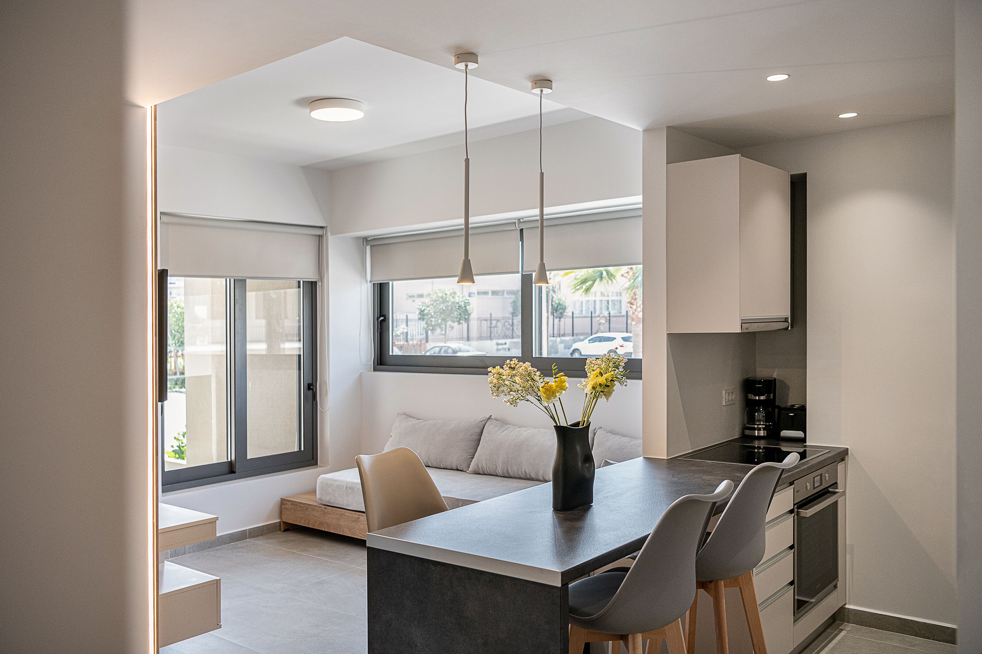 A modern kitchen with a built-in island, a dining area with chairs, and a large window providing a view of the street.