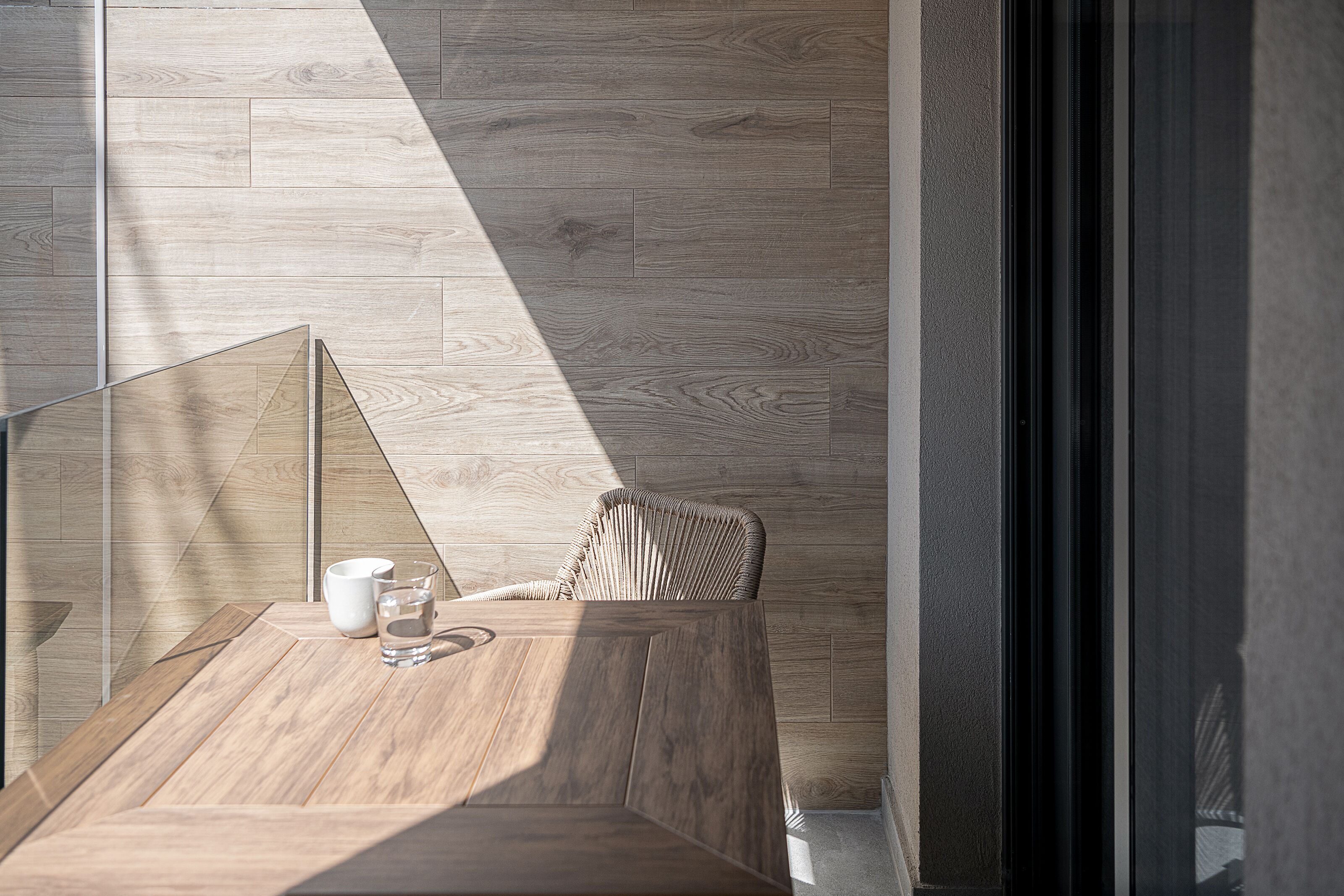 Una habitación moderna con suelo de madera, una pared divisoria de vidrio y una silla de mimbre.