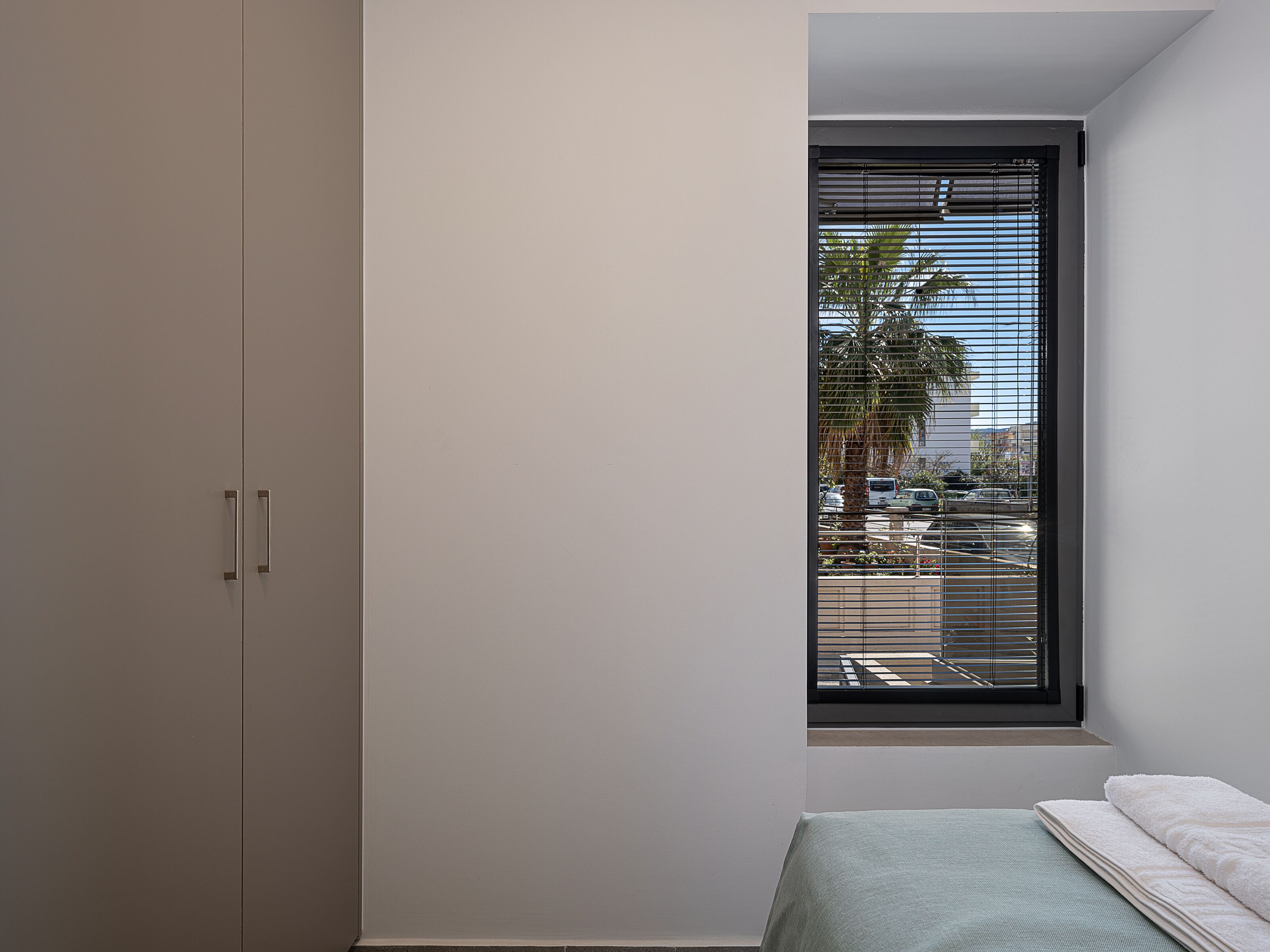A bedroom with a bed, a window with blinds, and a wardrobe.