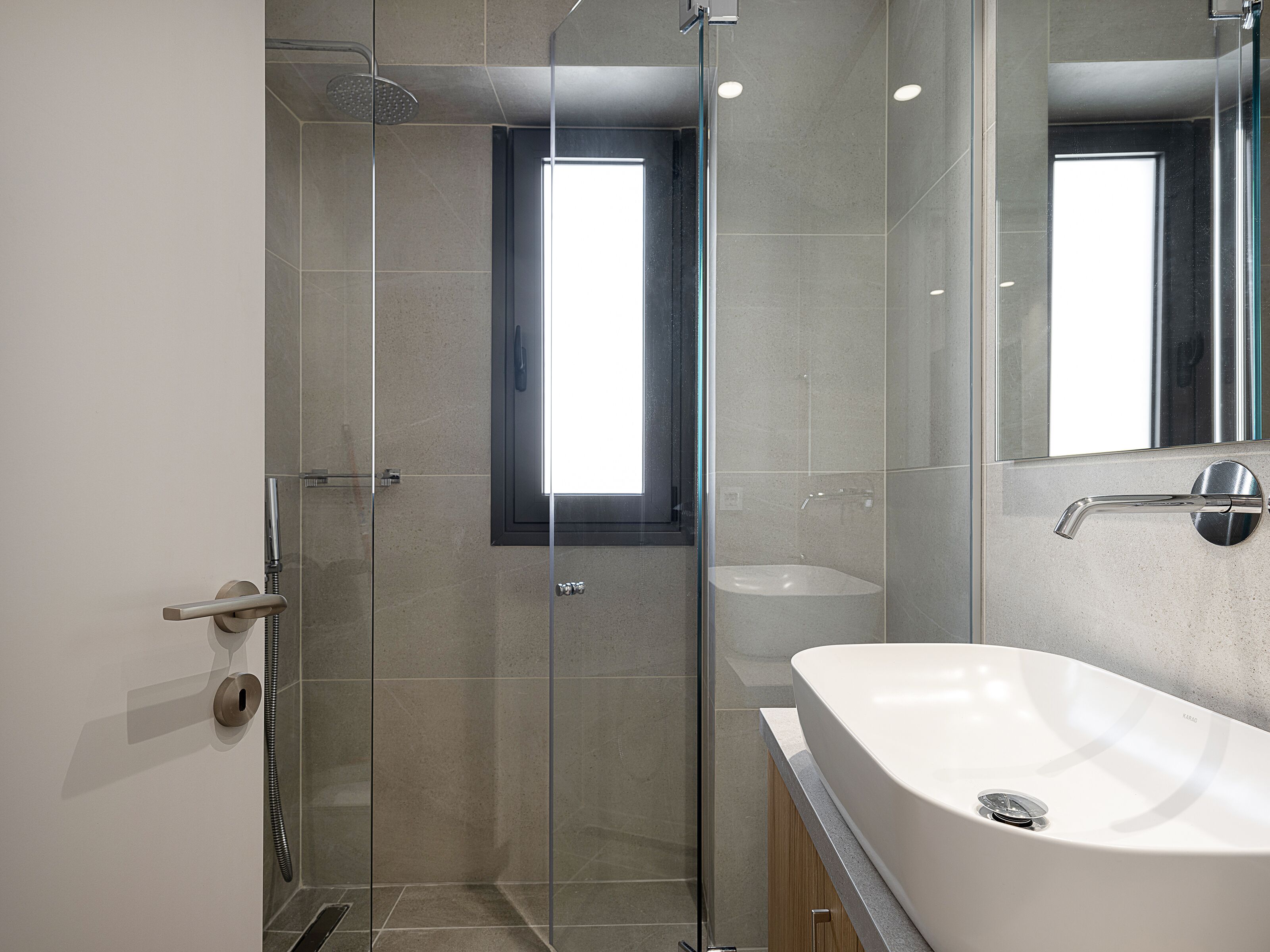 Un baño moderno con ducha envuelta en vidrio, una bañera grande y un espejo que refleja el cuarto.