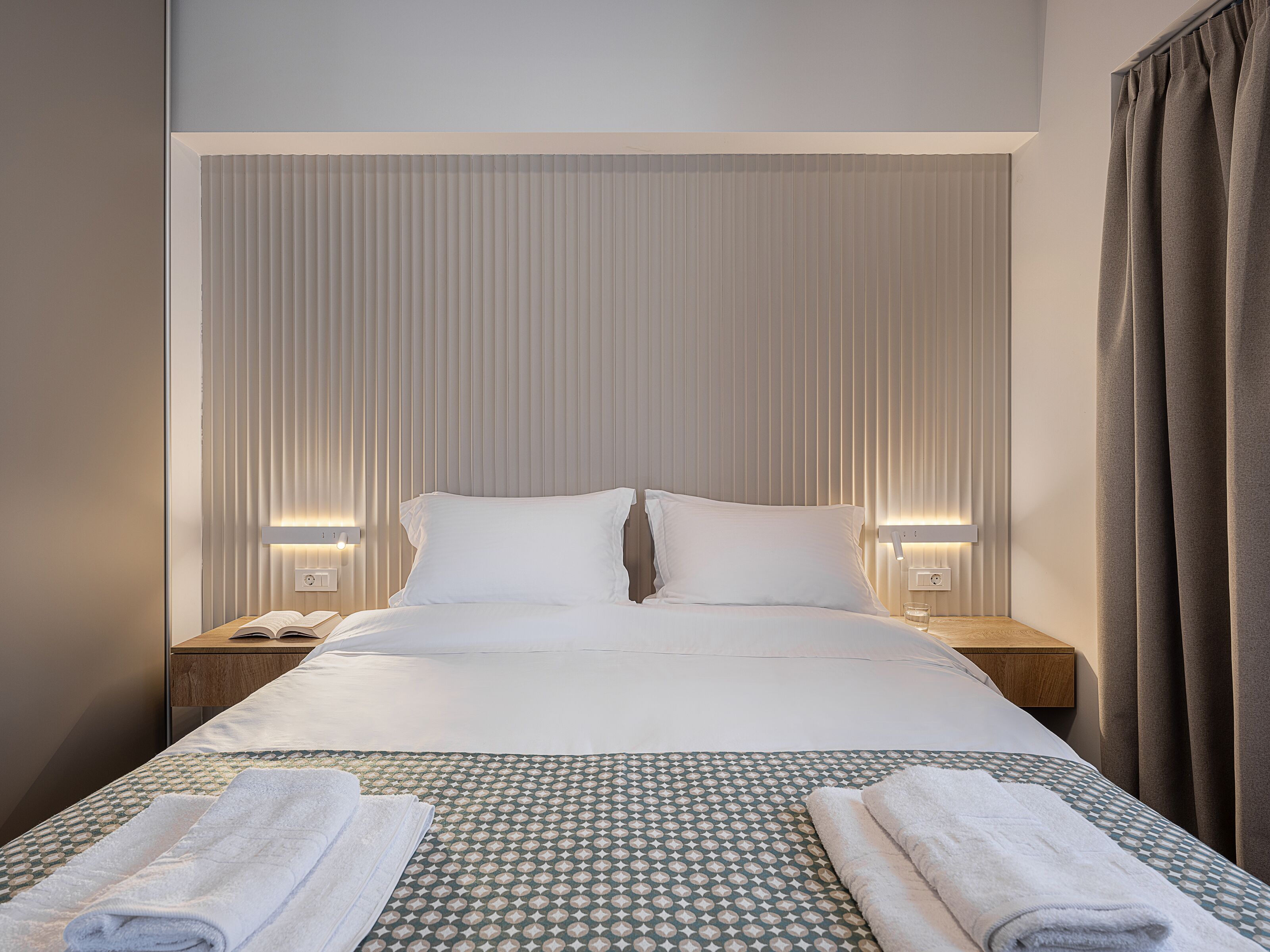 A neatly made bed with a patterned bedspread, two pillows, and two bedside lamps.