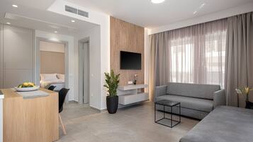 Una sala de estar moderna con un sofá gris, un comedor con una mesa de madera, y un televisor montado en la pared.