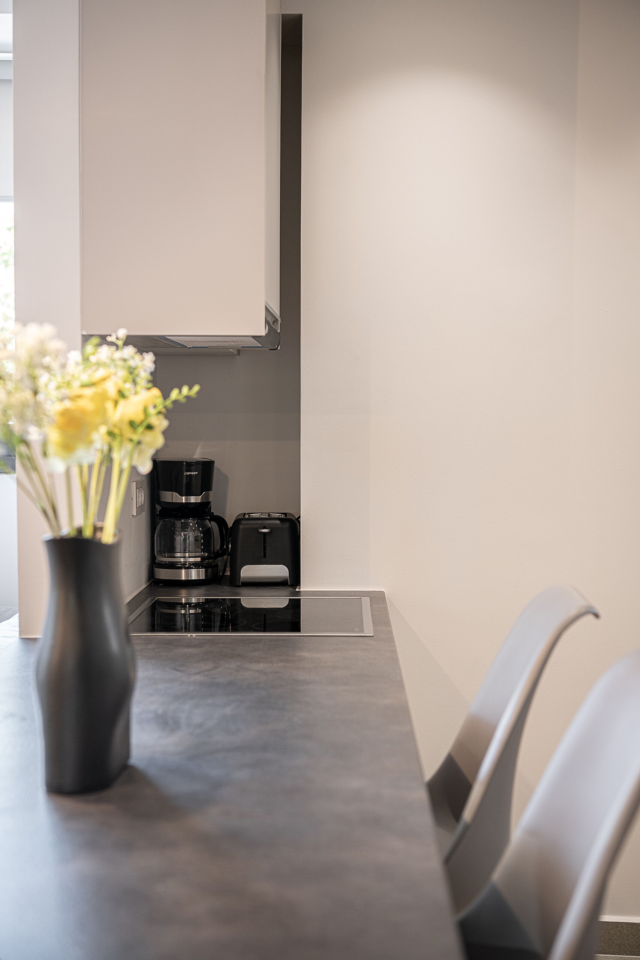 A modern kitchen with a coffee maker, toaster, and a vase with flowers on the counter.