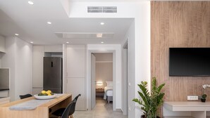 Uma cozinha moderna com geladeira embutida, área de refeições com mesa e cadeiras de madeira, uma planta grande em vaso e uma TV de tela plana fixada em uma parede de madeira.