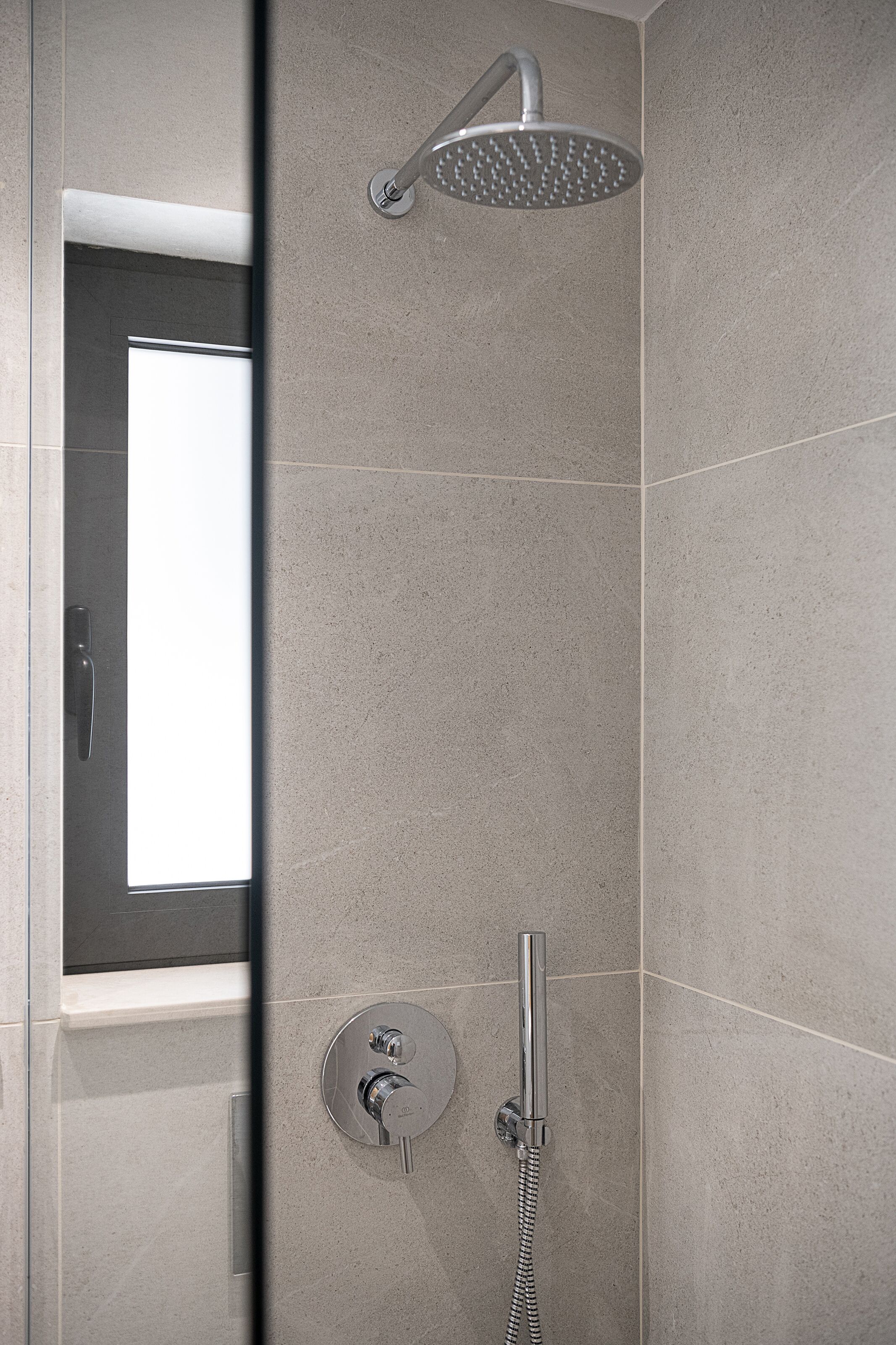 Een moderne douche met een handdouche en bediening op de muur.