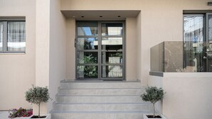 Entrada de um edifício com porta de vidro, degraus de concreto e dois vasos de plantas de cada lado.