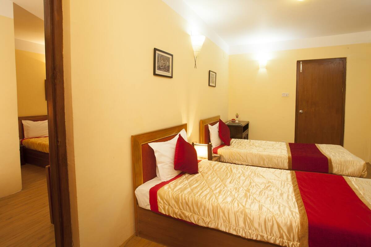 Habitación de hotel con dos camas, cabeceros de madera, una mesita de noche y una puerta.