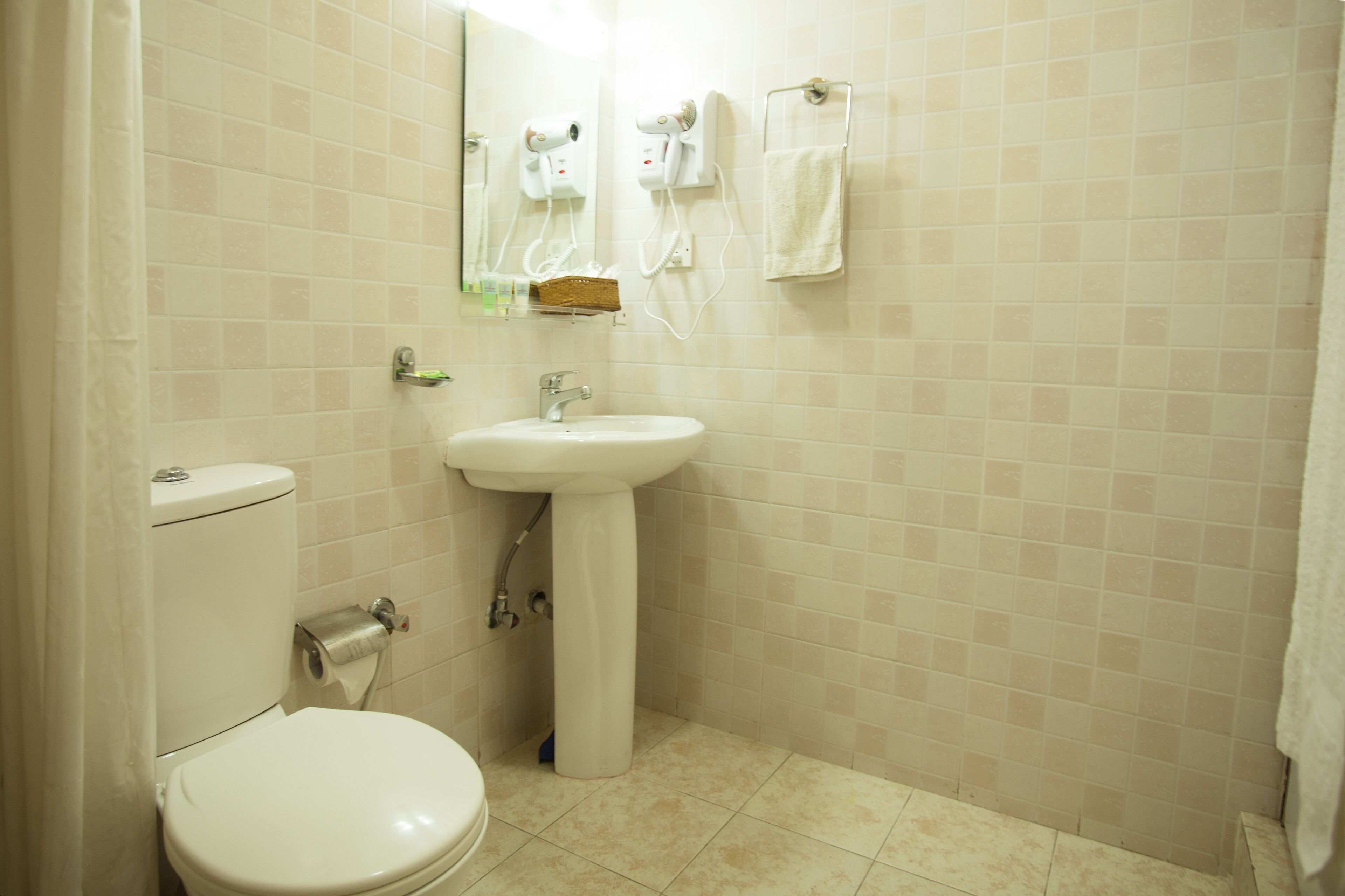 A bathroom with a toilet, sink, and hair dryers on the wall.