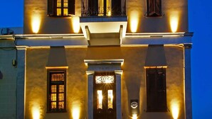 A two-story building with a balcony on the upper floor, a central entrance with a door, and multiple windows with shutters. - ARION HOTEL (Syros)