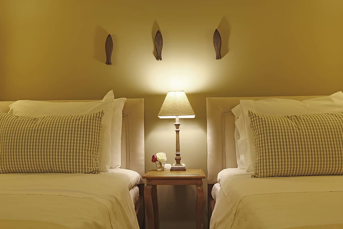 A hotel room with two beds, a nightstand with a lamp, and wall-mounted fish decorations.