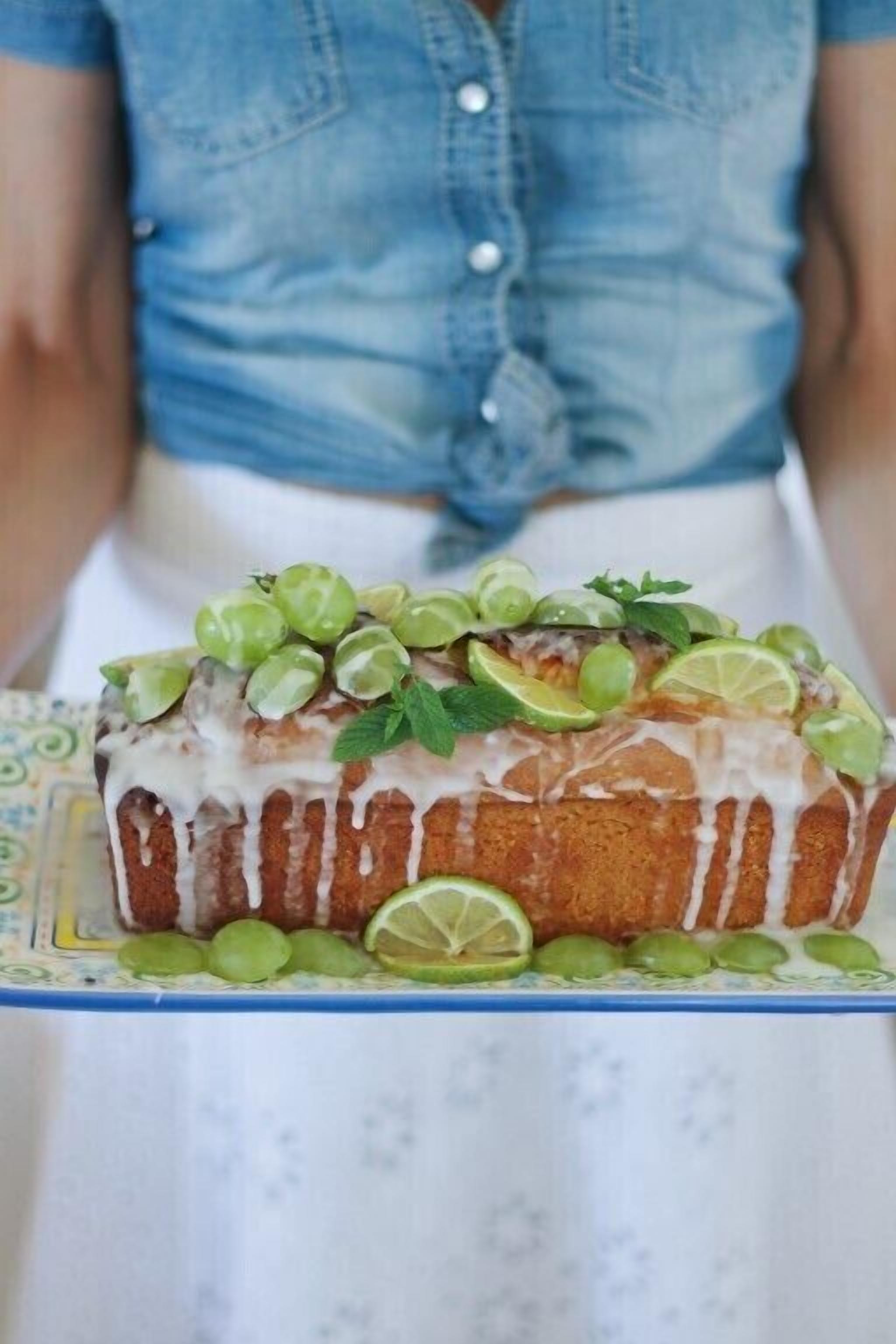 A loaf of bread with a white glaze, garnished with green grapes and mint leaves, placed on a patterned tray.