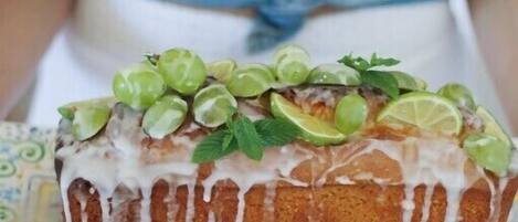 A loaf of bread with a white glaze, garnished with green grapes and mint leaves, placed on a patterned tray.