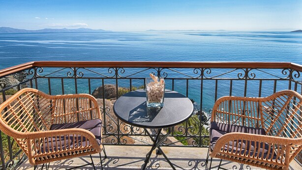 A balcony with wicker chairs and a small table, overlooking a vast body of water and distant mountains. - ARION HOTEL (Syros)
