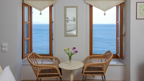 A room with a view of the sea, two wicker chairs, a small table with a vase of flowers, and a framed picture on the wall. - ARION HOTEL (Syros)