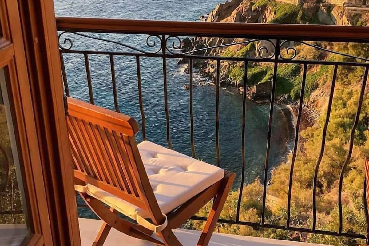 A balcony with a wooden chair and a view of the sea and rocky coastline.