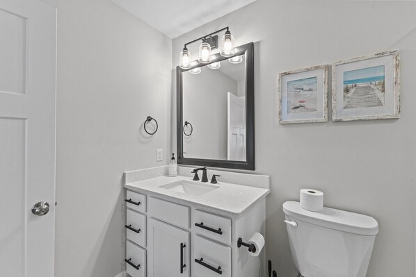 Une salle de bain avec un lavabo blanc, un miroir avec éclairage intégré, des toilettes et deux tableaux encadrés accrochés au mur.