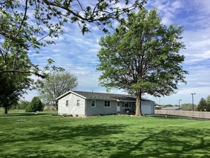 A single-story house with a front porch, surrounded by a well-maintained lawn and a large tree. - Enjoy golf course views with hot tub and fire pit. Three bedrooms, sleeps seven. (Altoona)