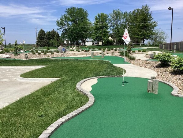 A miniature golf course with a green putting area, a parking lot, and surrounding landscaping. - Enjoy golf course views with hot tub and fire pit. Three bedrooms, sleeps seven. (Altoona)