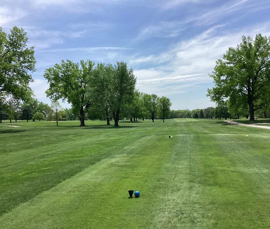 A well-maintained golf course with a clear sky, lush green grass, and trees in the background.