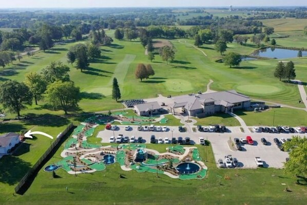 An aerial view of a golf course with a clubhouse, parking area, and a water park. - Enjoy golf course views with hot tub and fire pit. Three bedrooms, sleeps seven. (Altoona)