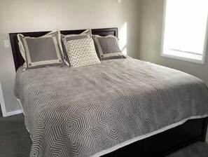 A bed with a geometric patterned bedspread, two pillows, and a dark headboard in a room with a window. - Enjoy golf course views with hot tub and fire pit. Three bedrooms, sleeps seven. (Altoona)