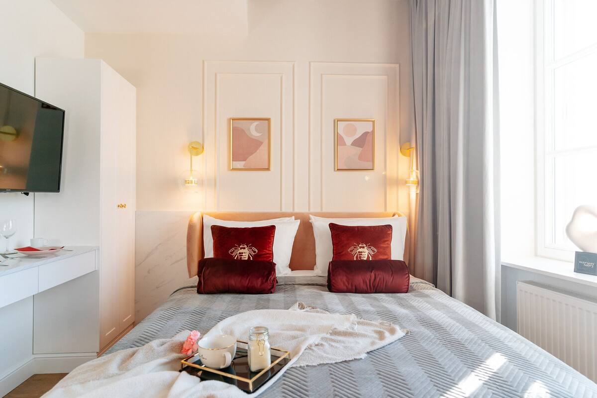Una habitación de hotel con una cama, televisor, escritorio y ventana con cortinas.