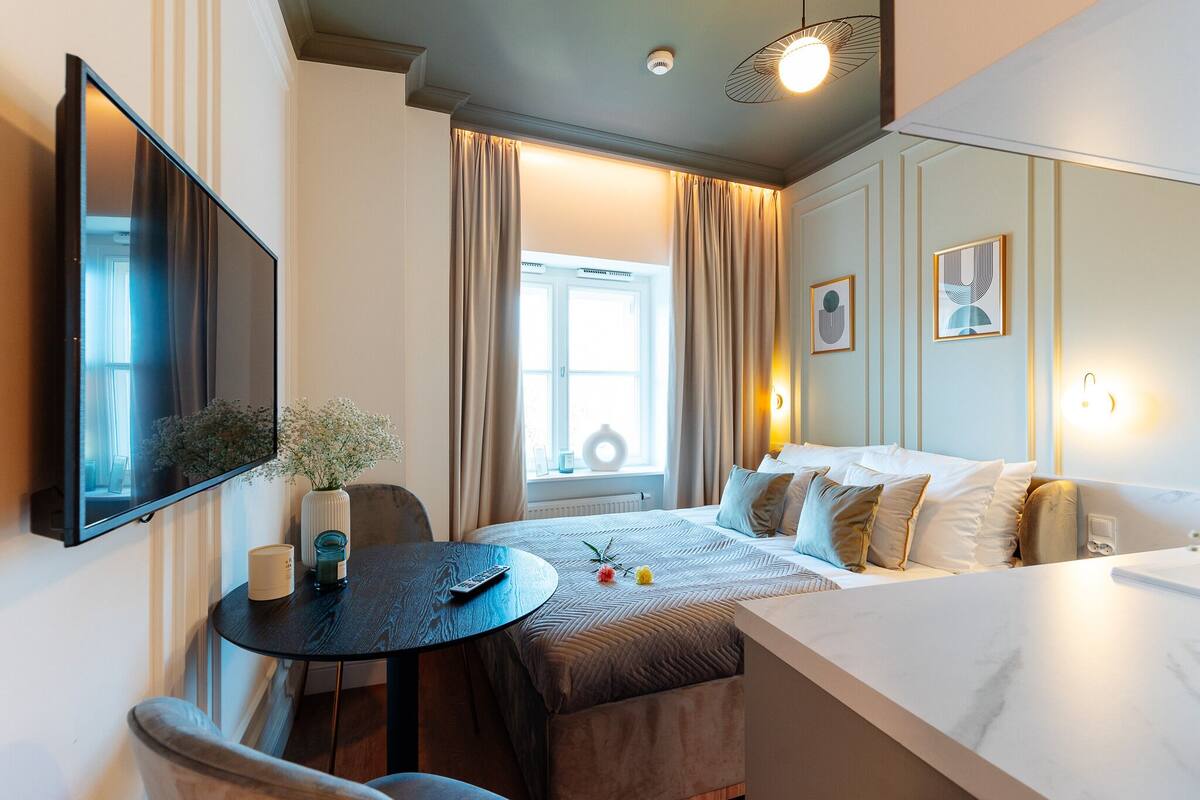 Una habitación de hotel moderna con cama, mesita de noche y un amplio ventanal con cortinas.