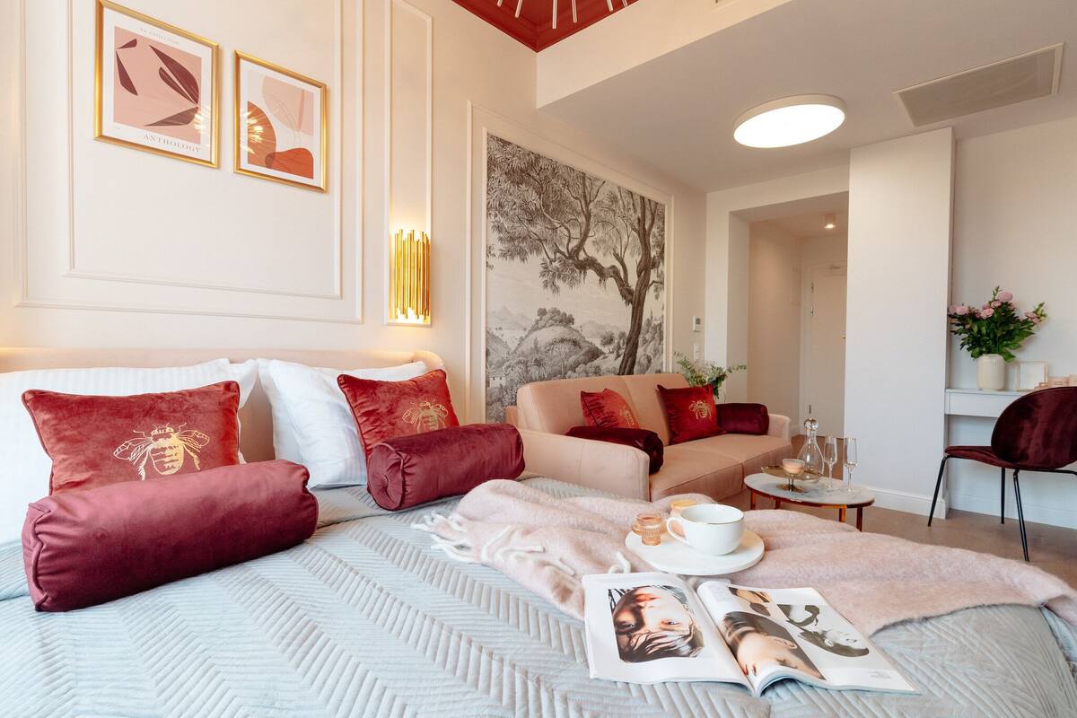 Una habitación de hotel con una cama, dos sofás, una mesa de comedor con vasos y una taza, y una pared decorada con cuadros.