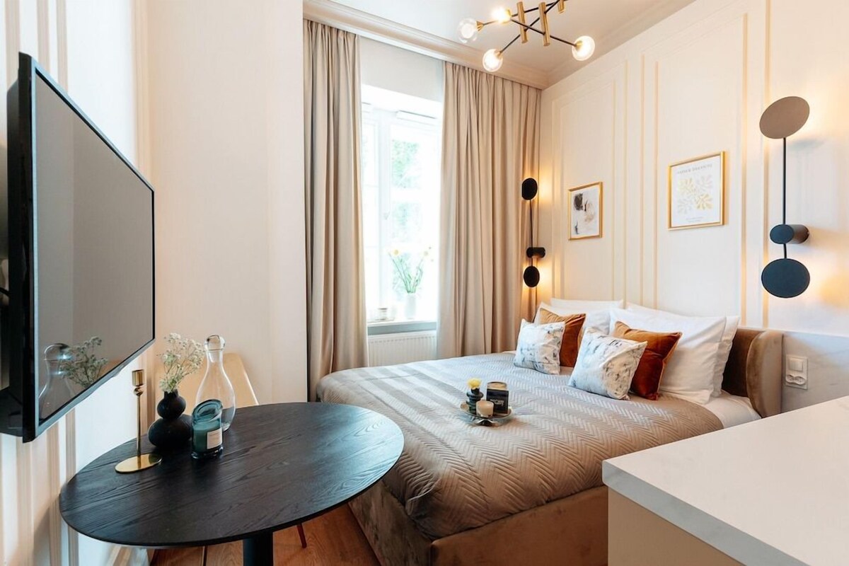 Habitación de hotel con cama, mesita de noche, lámpara y un espejo grande.