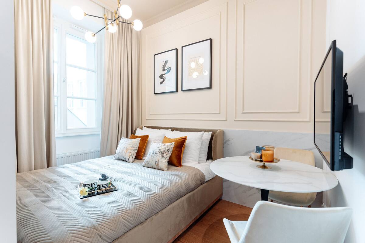 Una habitación de hotel con una cama, una mesa redonda con una vela y dos cuadros en la pared.