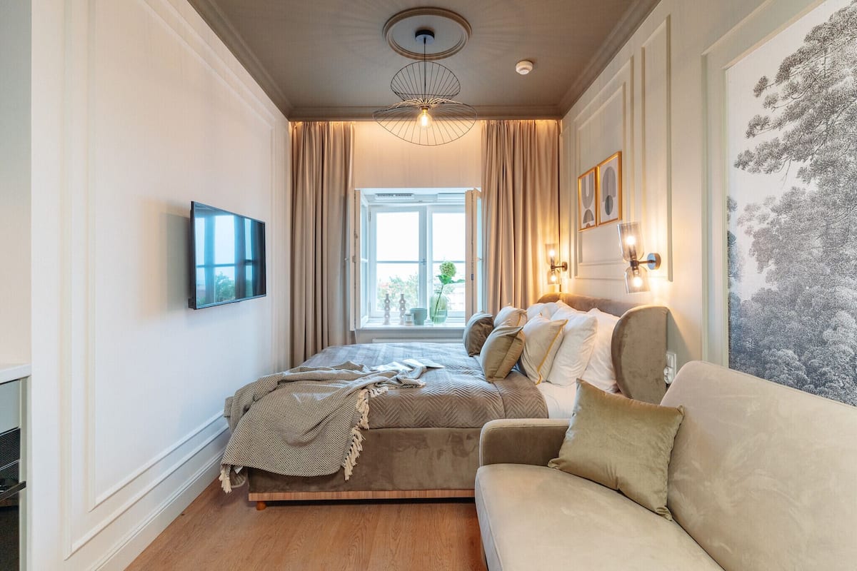 Un dormitorio con cama, sofá, televisor y ventana con cortinas.