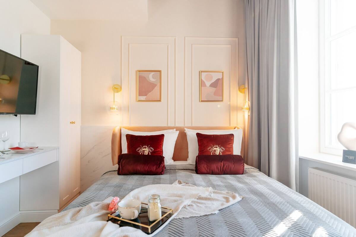 Habitación de hotel con cama, mesitas de noche, televisor, obras de arte en la pared y ventana con cortinas.