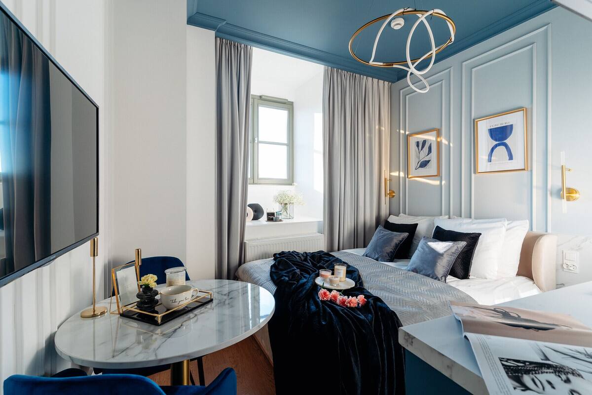 Una habitación de hotel moderna con cama, mesita de noche y un ventanal con cortinas.
