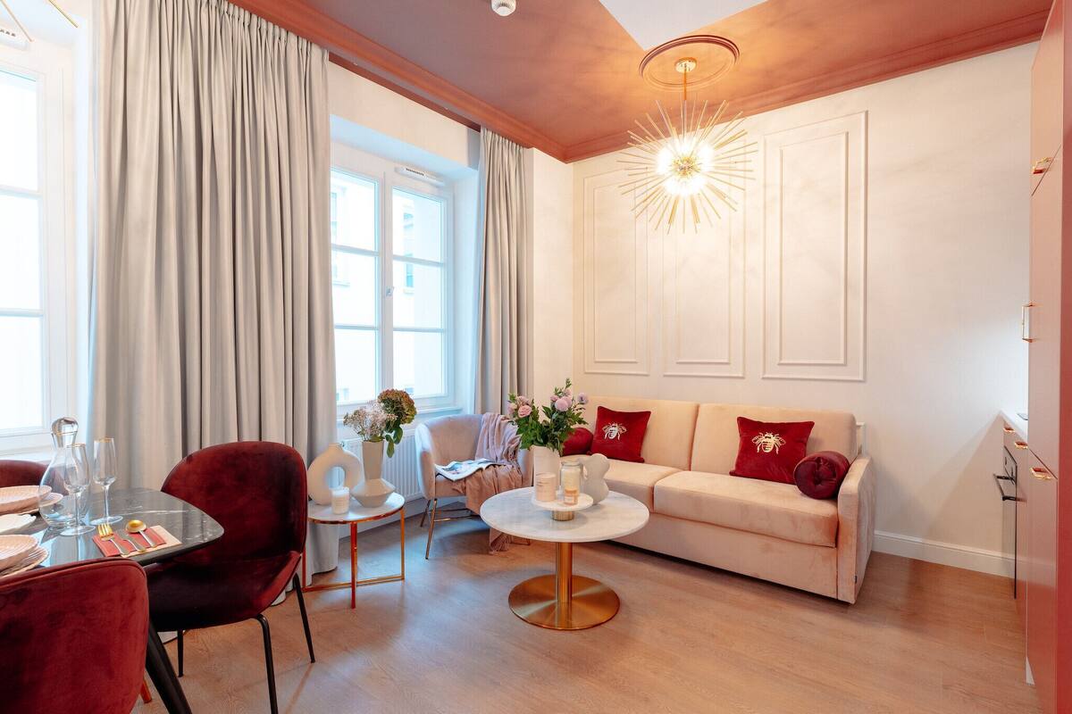 Un salón bien iluminado con un sofá, sillas rojas, una mesa de centro y un comedor con una mesa dispuesta para dos personas.