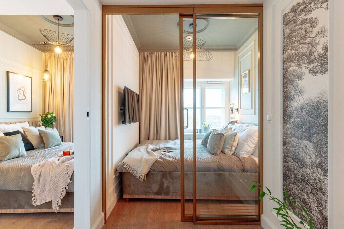Un dormitorio moderno con puerta corredera de vidrio que da a otra habitación, cama con una paleta de colores neutros y televisor montado en la pared.